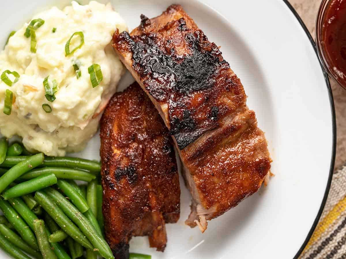 Cut ribs on a white plate with mashed potatoes and green beans.