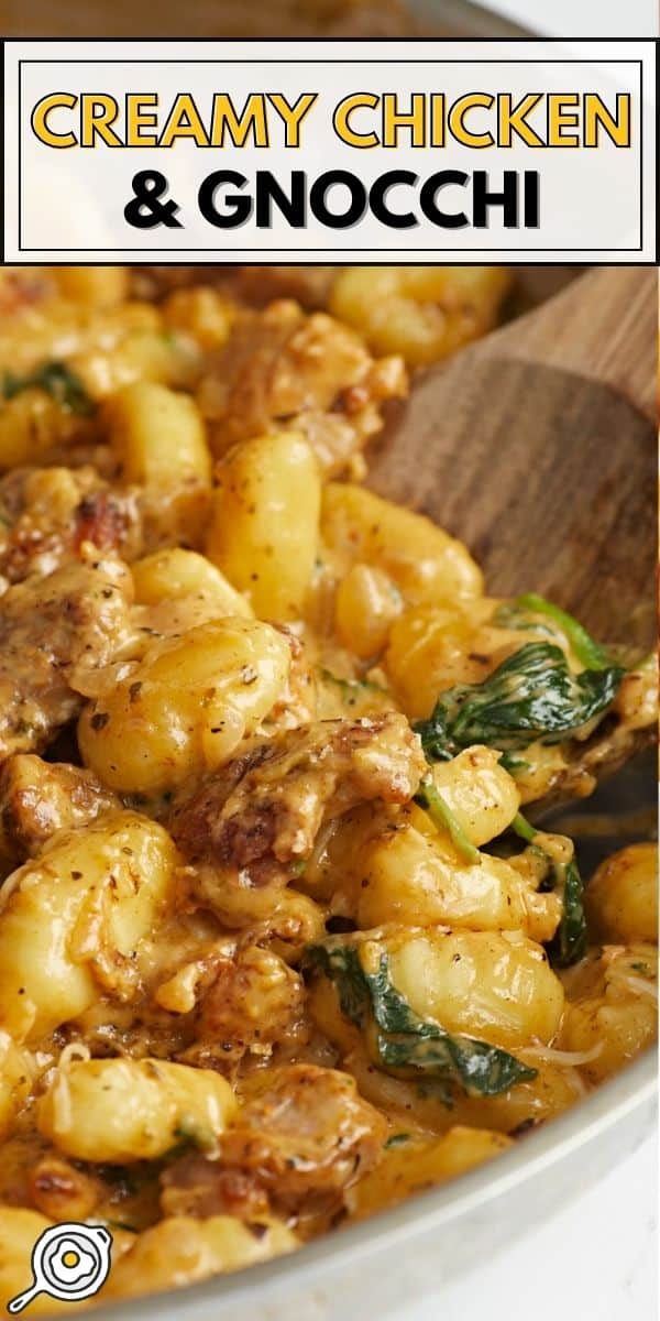 Side shot of Creamy Chicken and Gnocchi in a silver skillet with a wooden spoon in it.