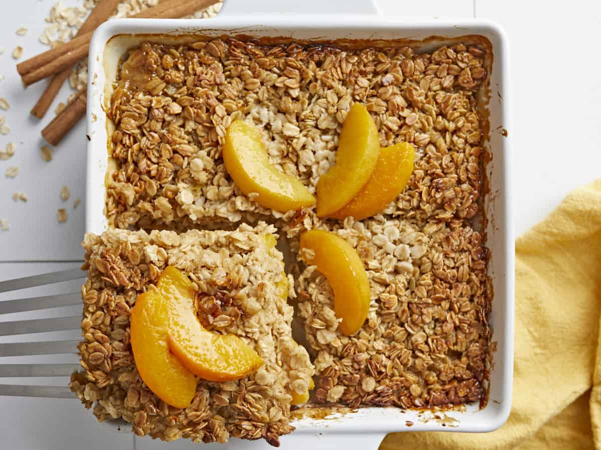 Overhead shot of a portion of Peach Baked Oatmeal being lifted out of a white baking dish.