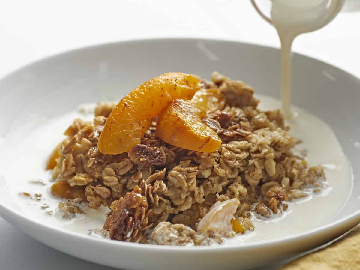 Side shot of Peach Baked Oatmeal in a white bowl with cream being poured into it.