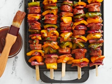Sausage Kebabs on a grill pan with a bowl of BBQ sauce on the side.