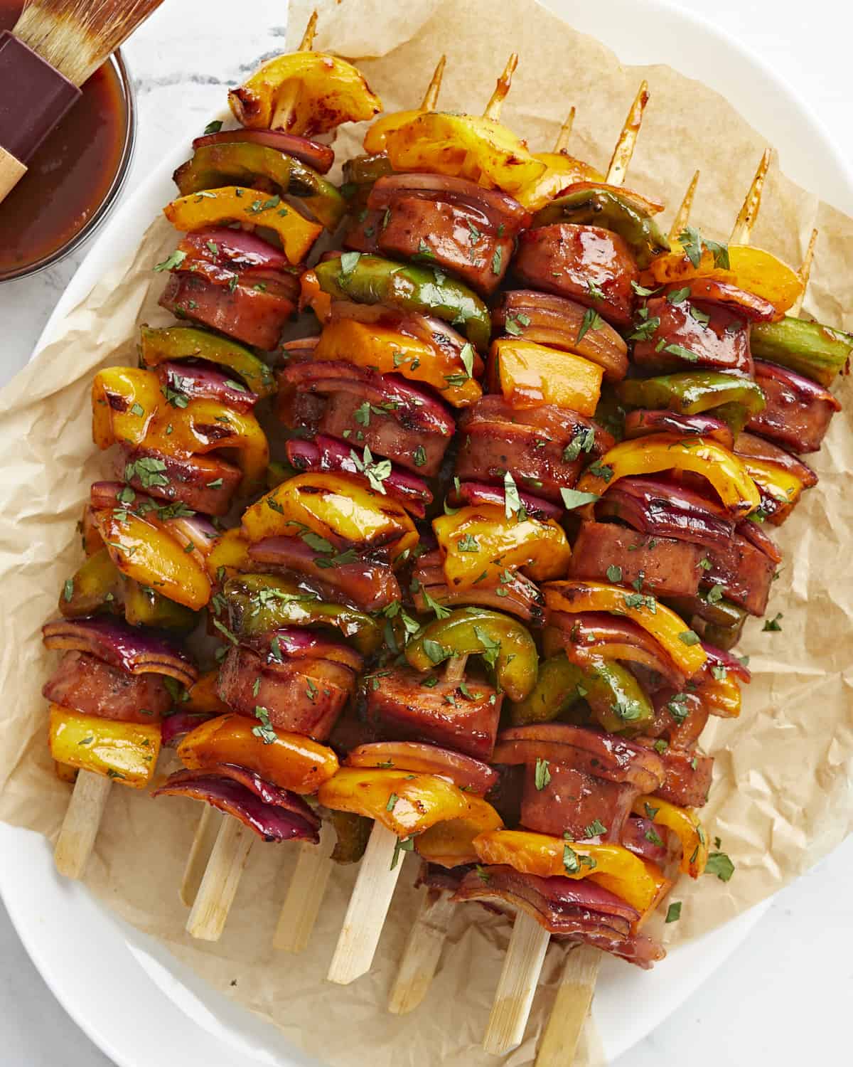 Overhead view of sausage kebabs on a serving platter with parchment paper.