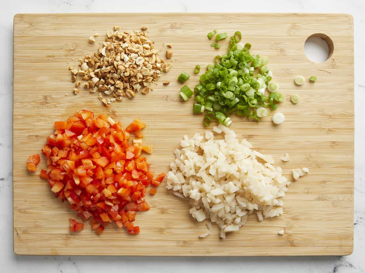 Chopped bell pepper, water chestnuts, green onions and peanuts on a wood cutting board.