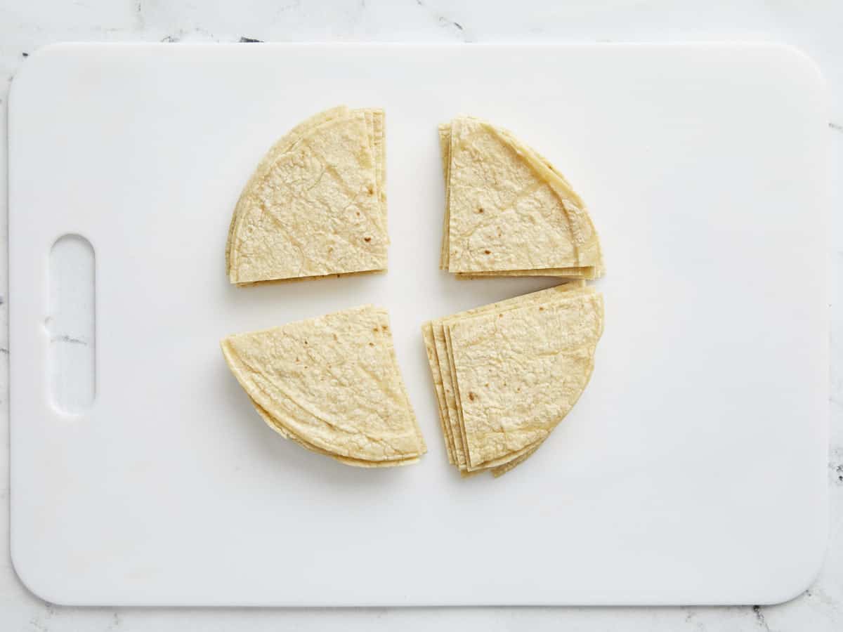Overhead shot of quartered tortillas on a white cutting booard.