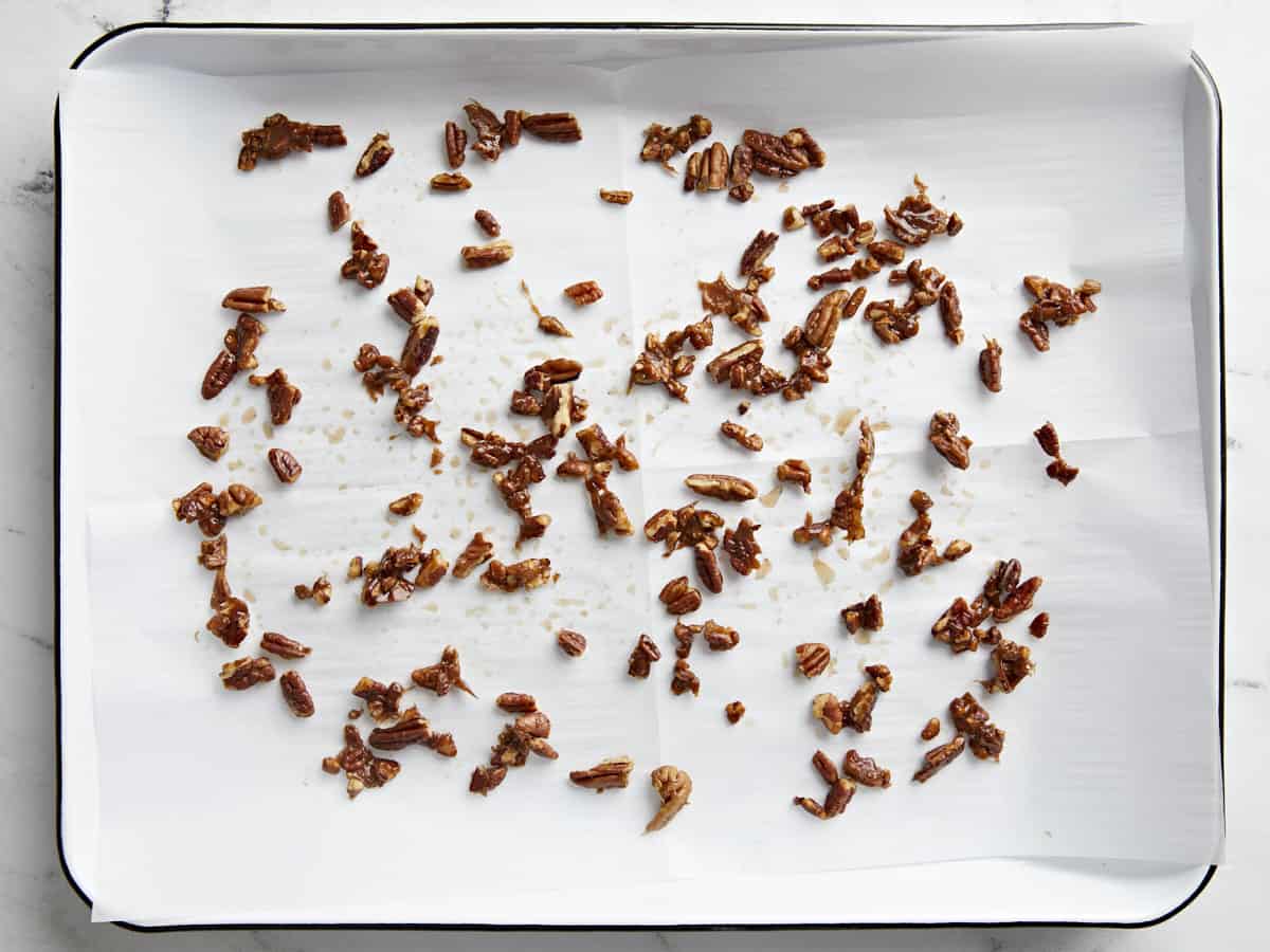 Candied pecans spread out on a parchment lined baking sheet