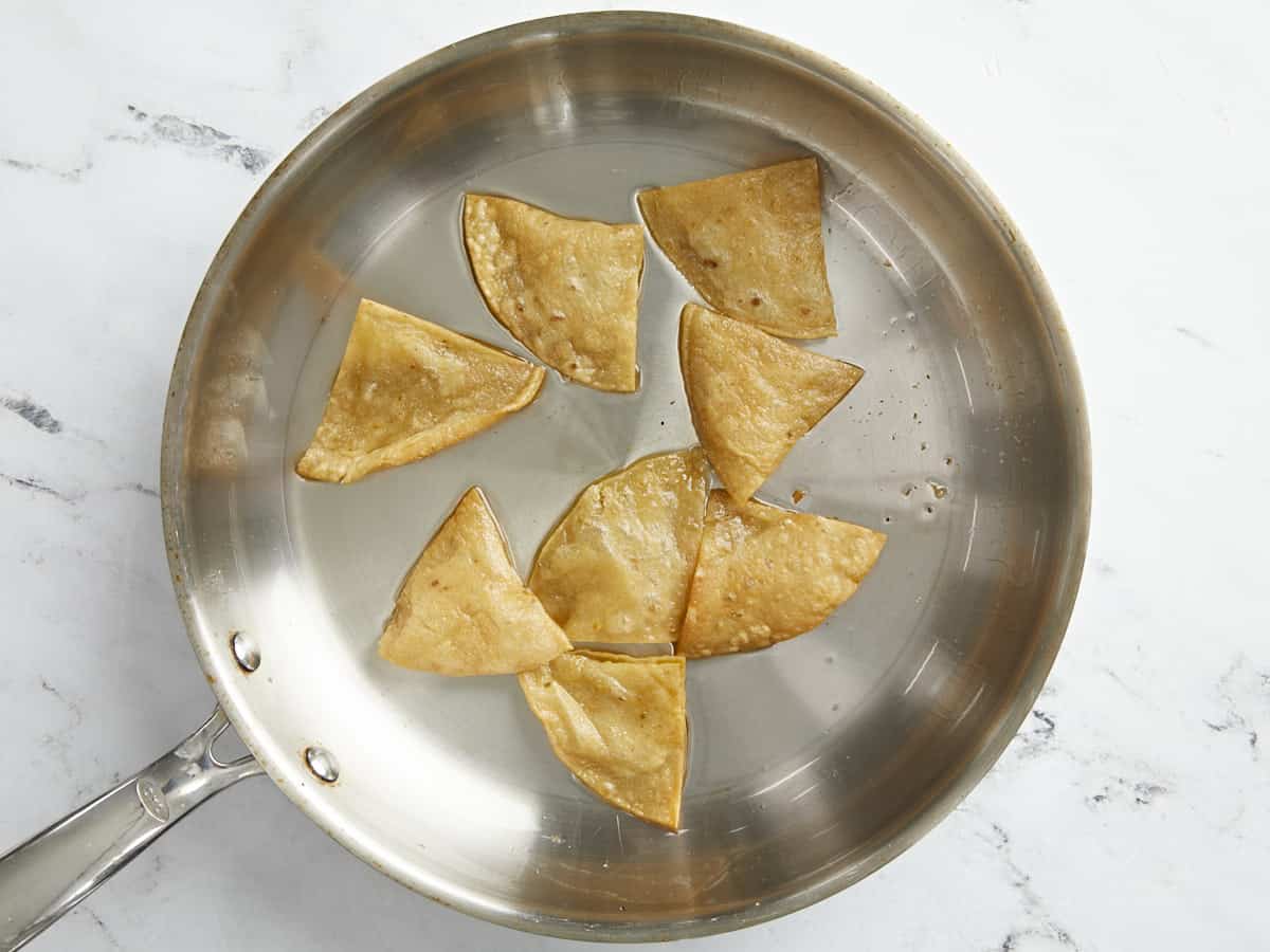 Overhead shot of tortilla slices being fried in a silver pan.