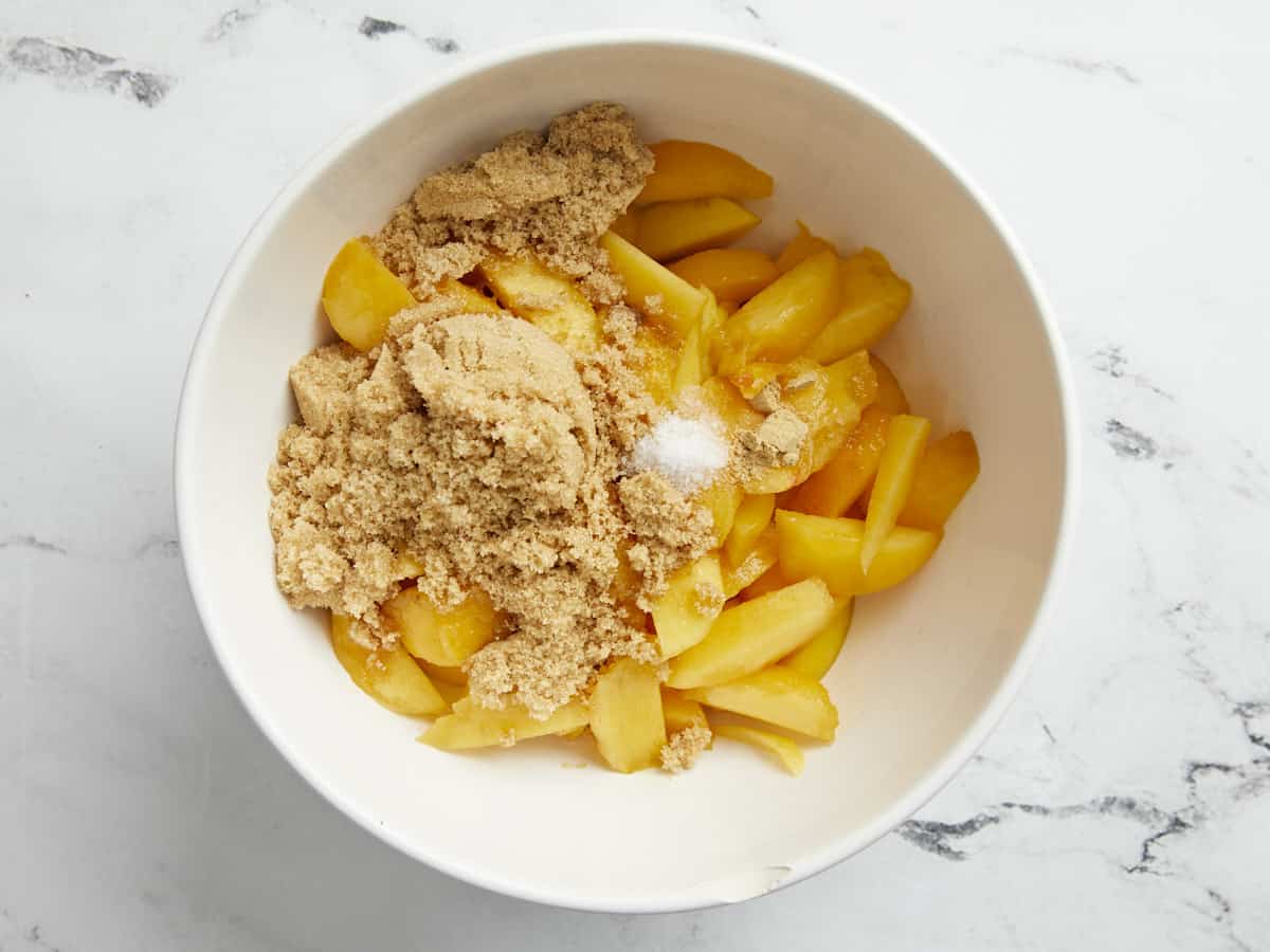 Overhead shot of peaches and brown sugar with other filling ingredients in a white bowl.