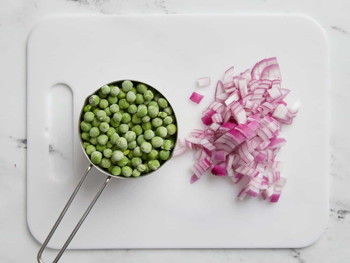 Diced red onion and a measuring cup full of frozen peas.