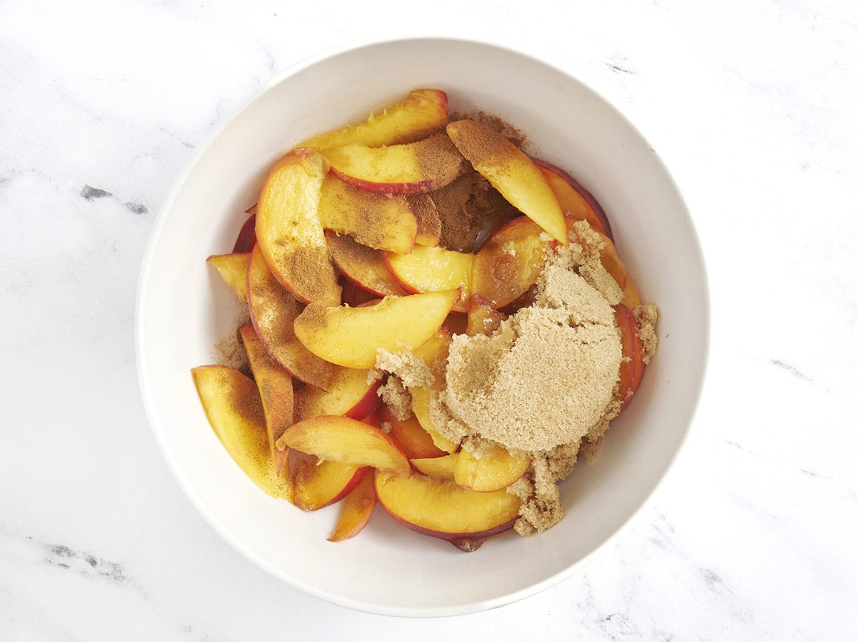 Brown sugar and cinnamon added to fresh peaches in a bowl.