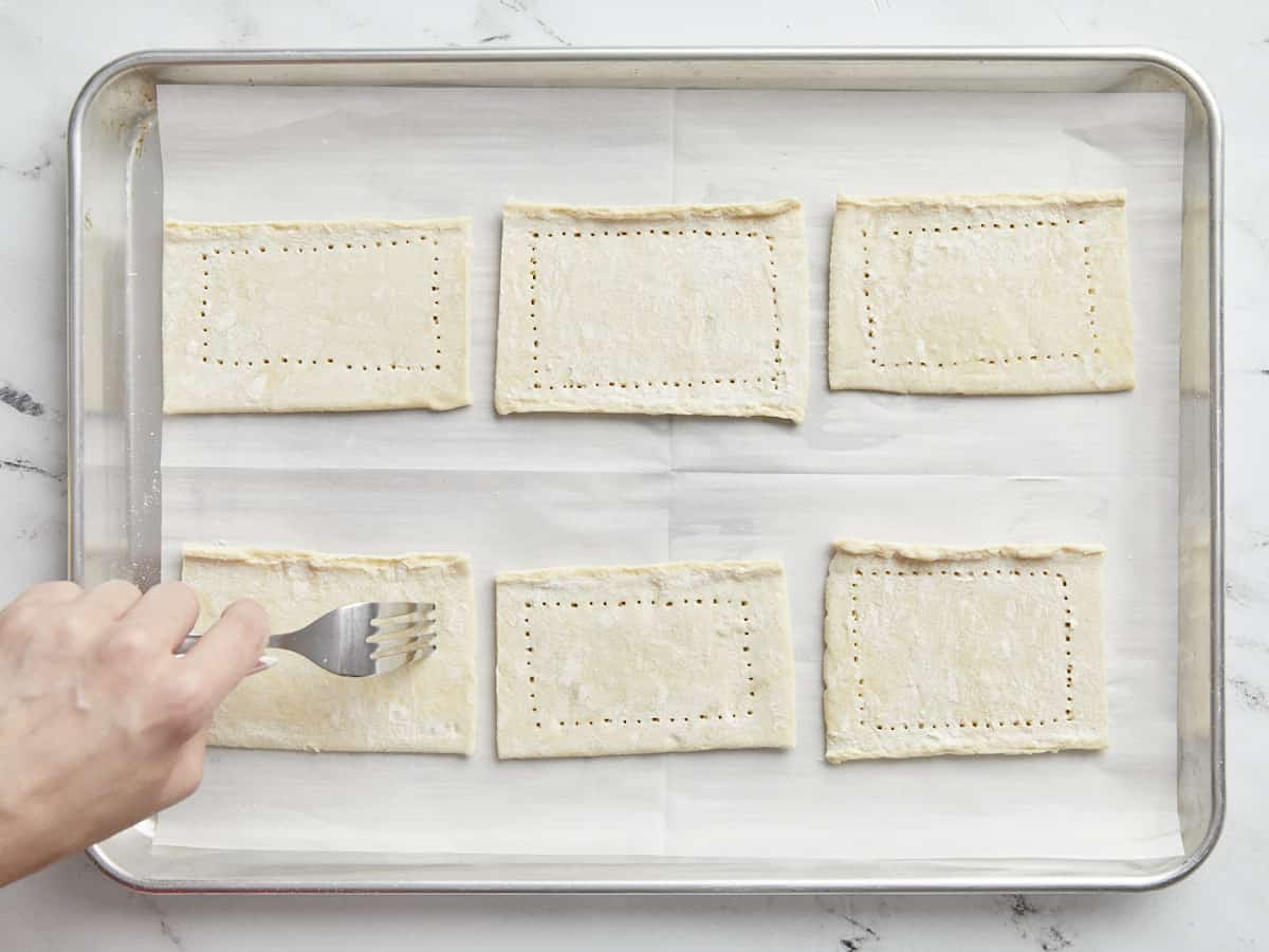 Overhead shot of puff pastry rectangles being docked with a fork.