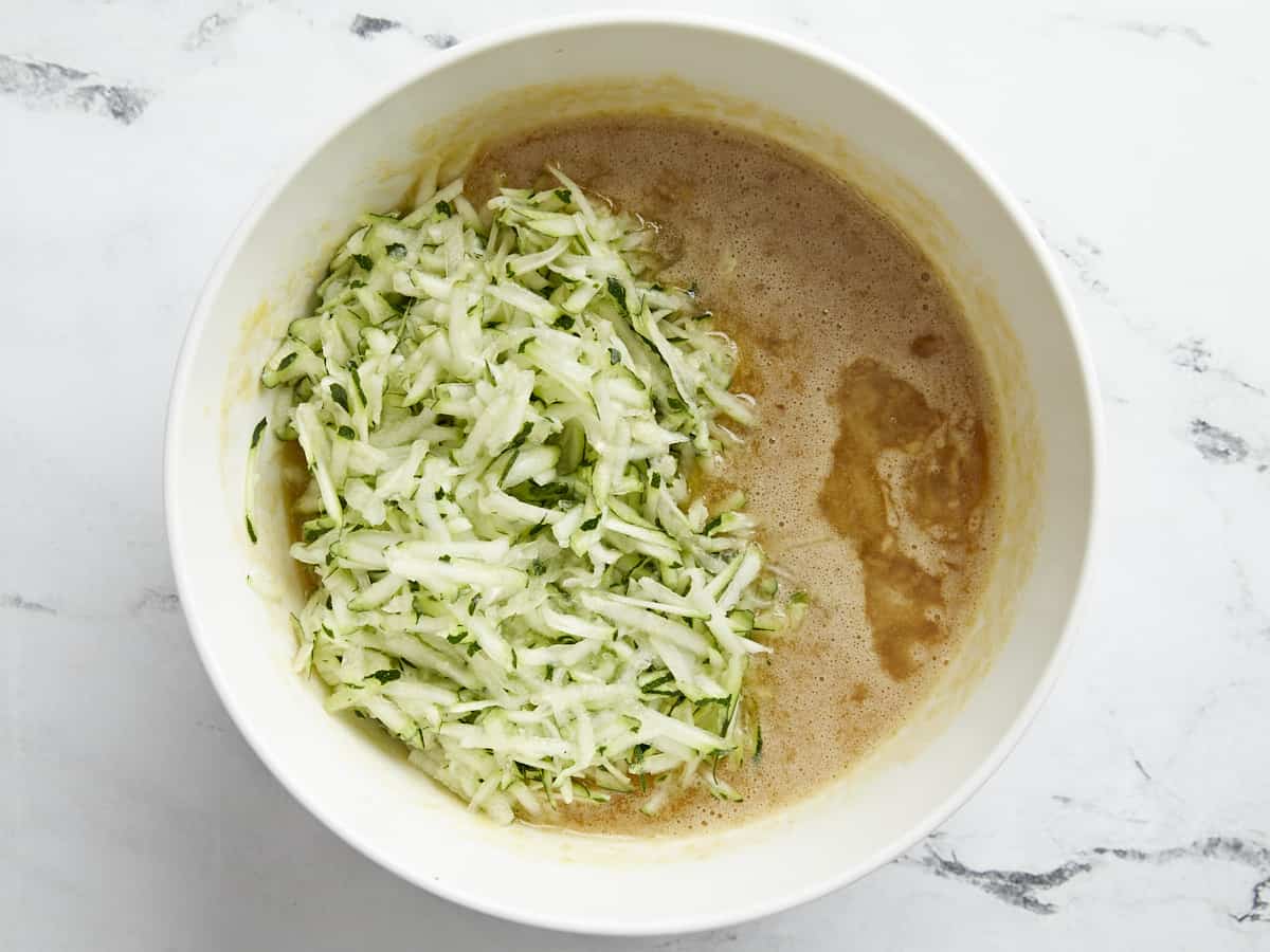 Shredded zucchini added to wet ingredients bowl