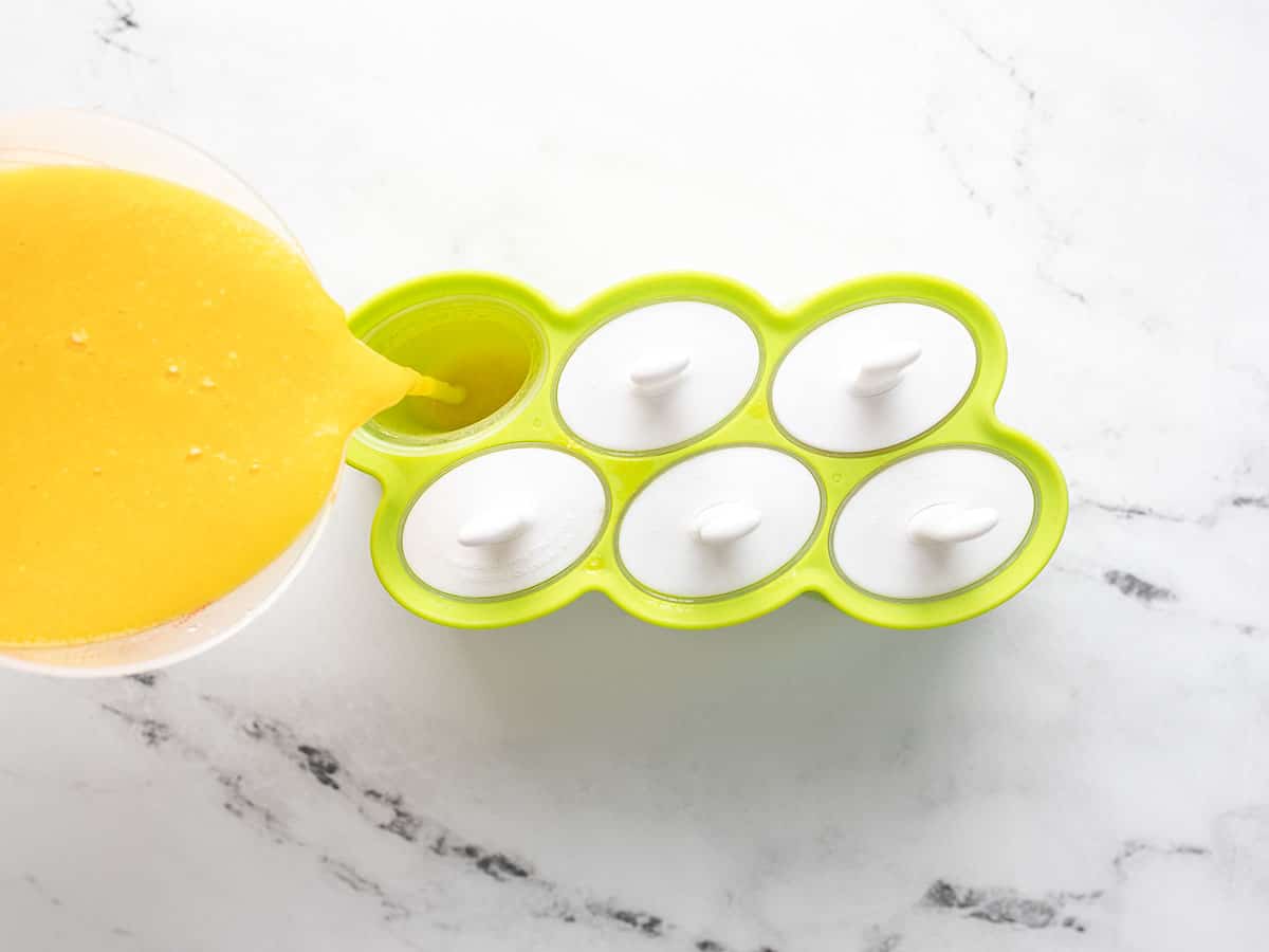 Overhead shot of mango puree being poured into popsicle molds.