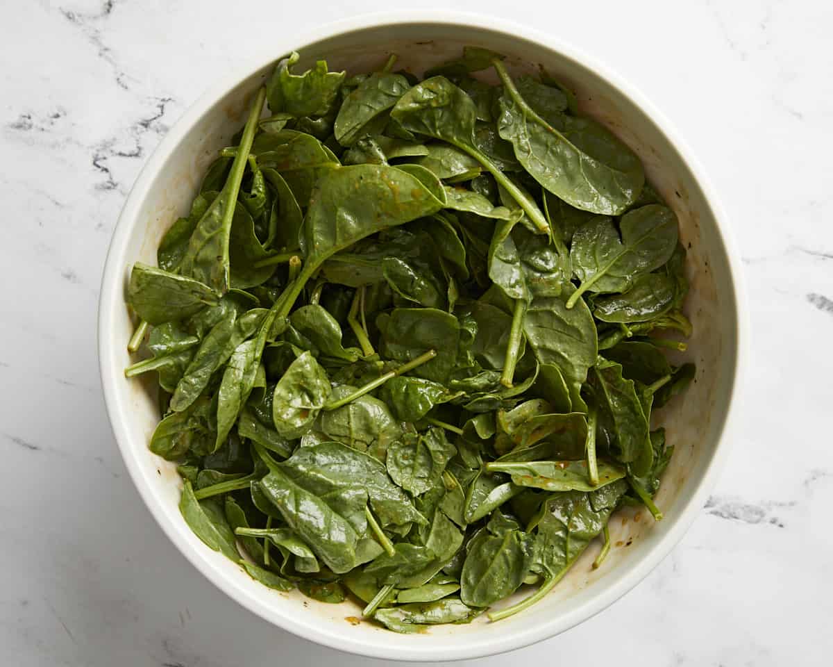 Baby spinach in a large serving bowl with balsamic vinaigrette dressing