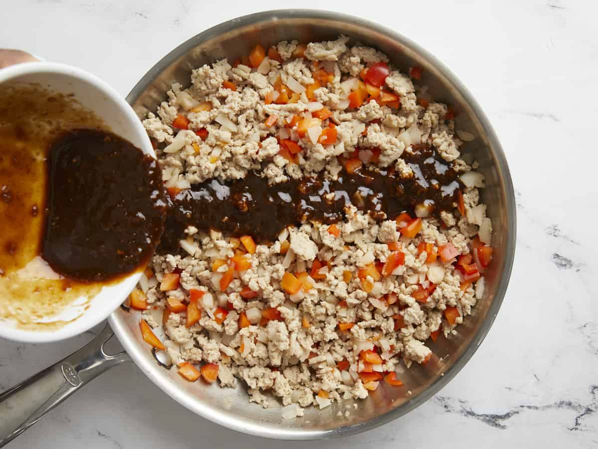 Asian sauce mixture being poured over cooked chicken and vegetables.