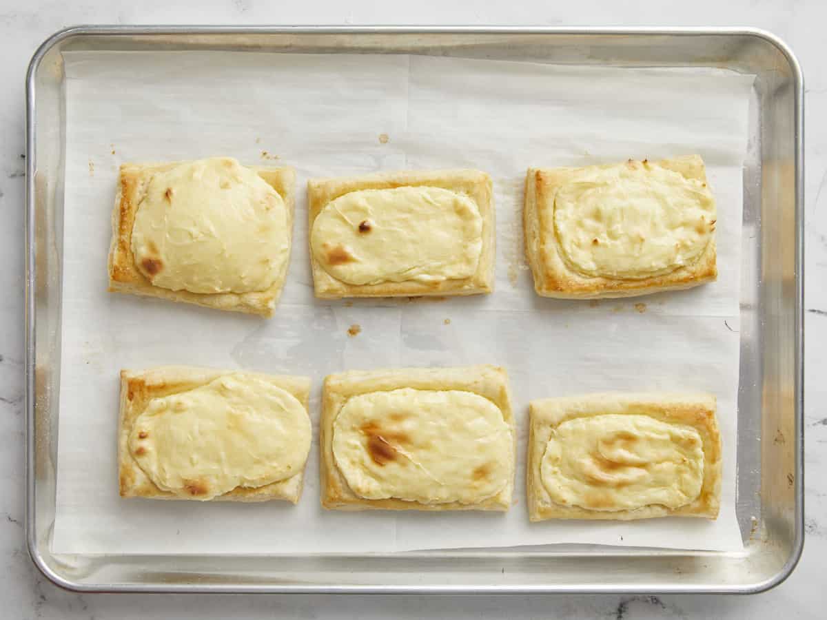 Overhead shot of 6 baked cheese danish on.a sheet pan.