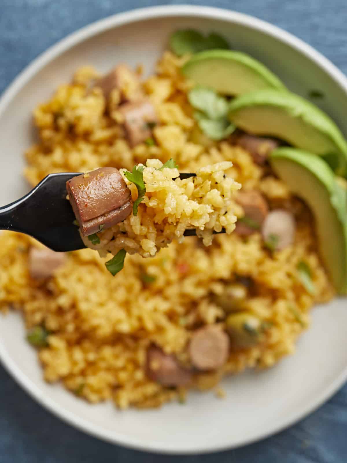 Overhead shot of Arroz Con Salchichas on a plate in the background with a fork holding some in the foreground.