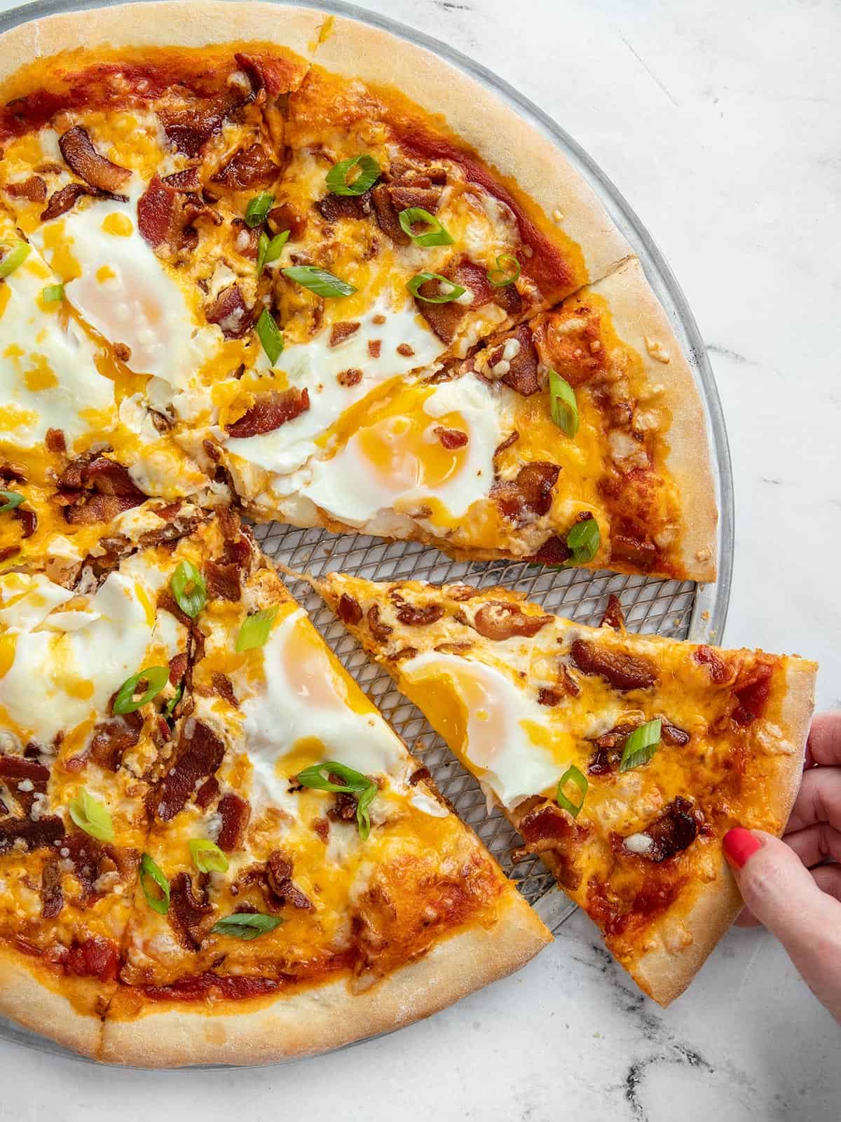 One slice of breakfast pizza being pulled from the pie.