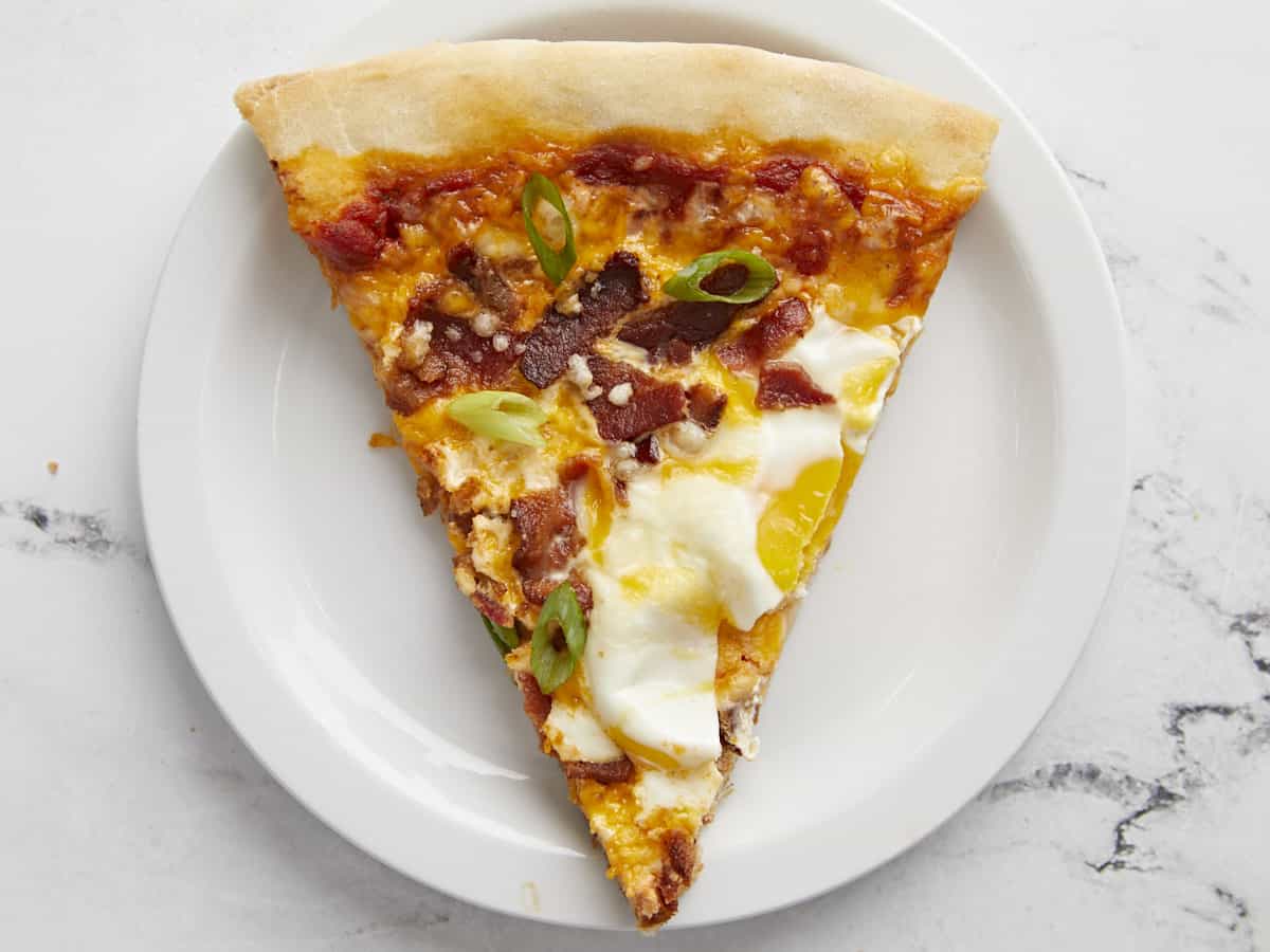 Overhead view of one slice of breakfast pizza on a plate.