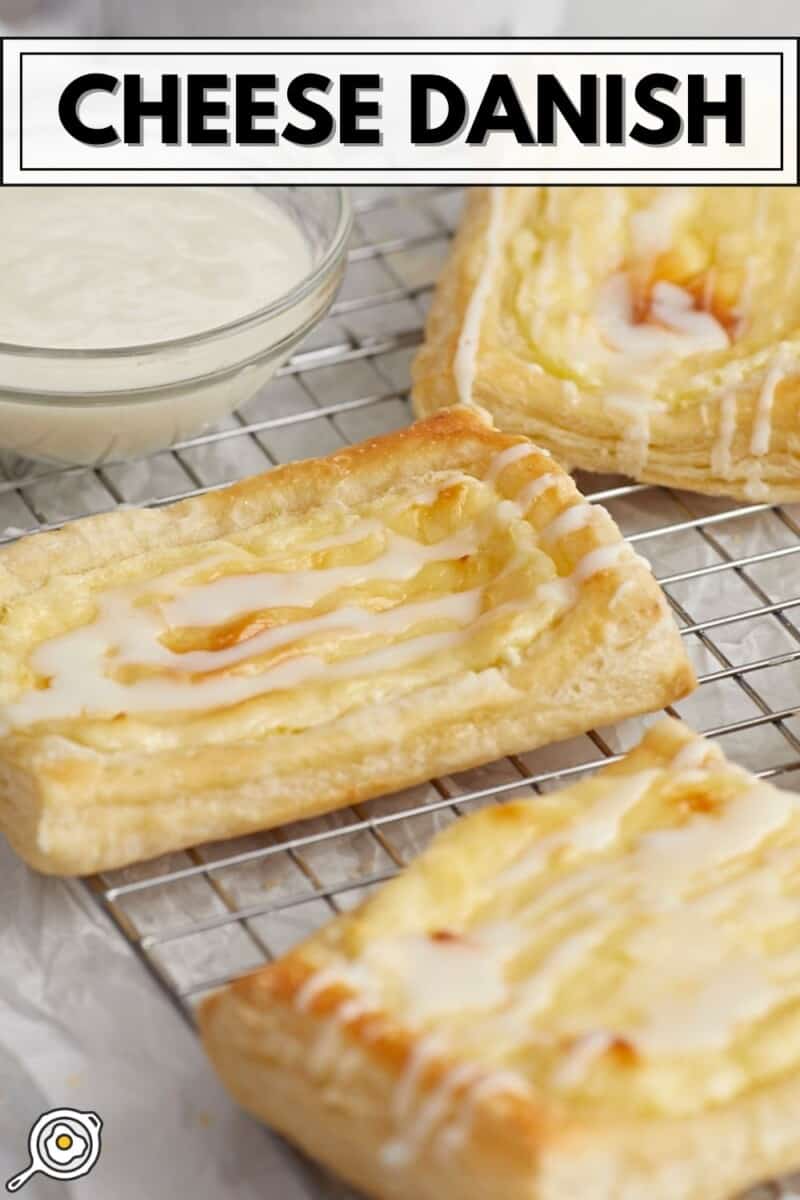 Side shot of cheese danish on a cooling rack with a small bowl of icing next to them.