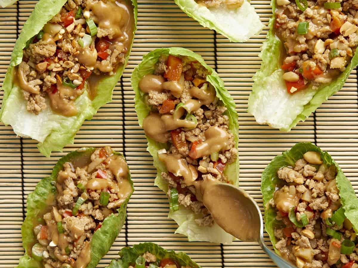 Very close up shot of chicken lettuce wraps being drizzled with peanut lime dressing.