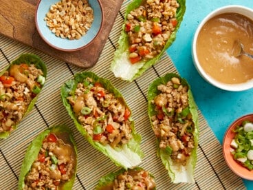 Overhead shot of chicken lettuce wraps with bowls of chopped peanuts, chopped green onions and peanut lime dressing on the side.