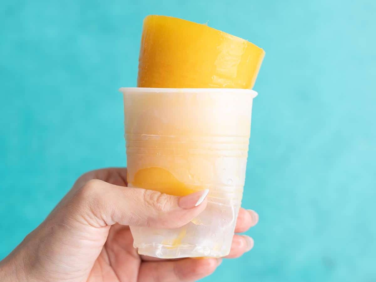 Side shot of hand holding a plastic cup with a mango limber poking out of it.