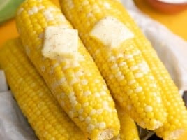 Overhead shot of cobs of Microwave Corn On The Cob on a black plate with two pats of butter melting on top.