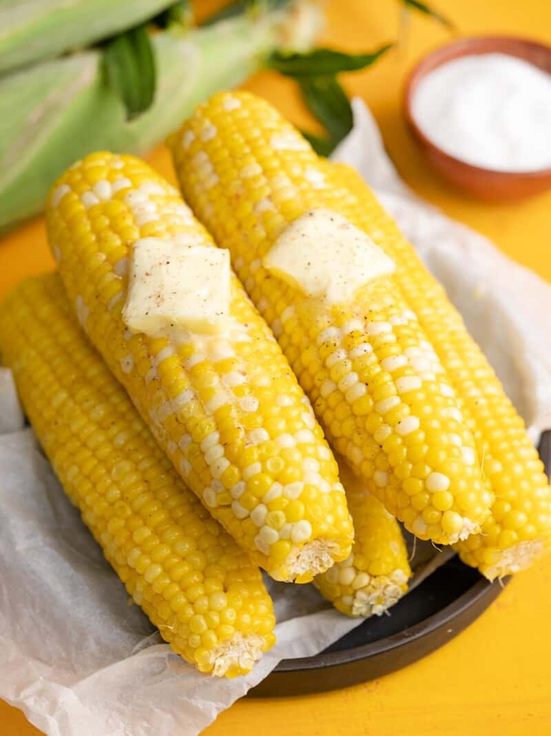 Overhead shot of cobs of Microwave Corn On The Cob on a black plate with two pats of butter melting on top.