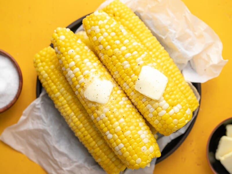 Overhead shot of cobs of Microwave Corn On The Cob on a black plate with two pats of butter melting on top.