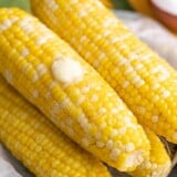 Side shot of cobs of Microwave Corn On The Cob on a black plate with a pat of butter melting on top.