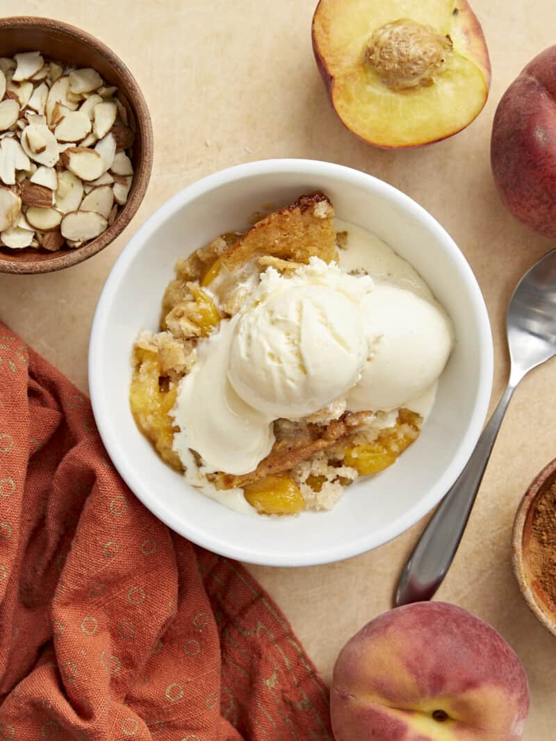 Overhead shot of a scoop of peach cobbler in a white bowl topped with a scoop of vanilla ice cream.
