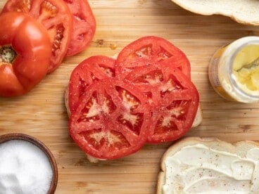 Overhead view of a tomato sandwich being built on a wooden cutting board.