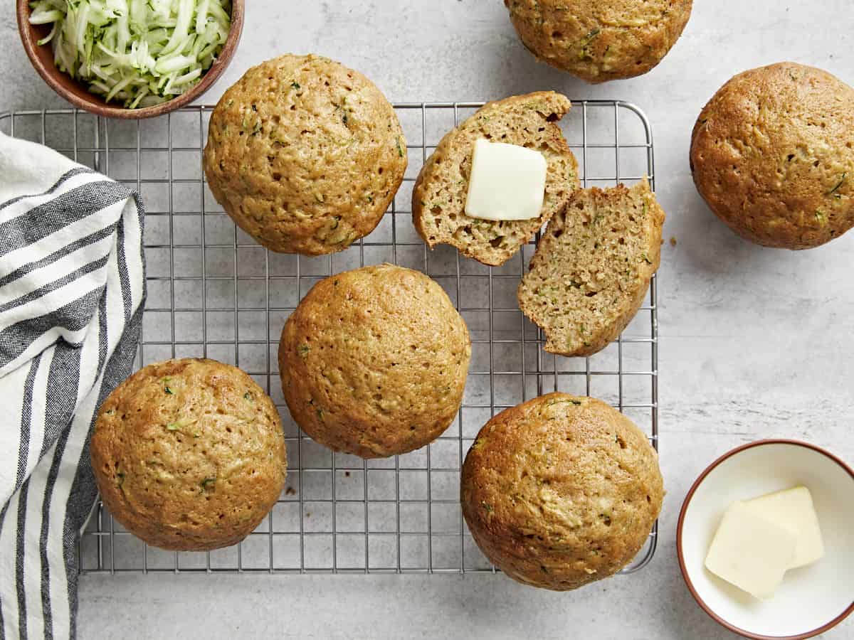 Overhead view of Zucchini muffins on a wire rack with one cut open and butter spread on top.