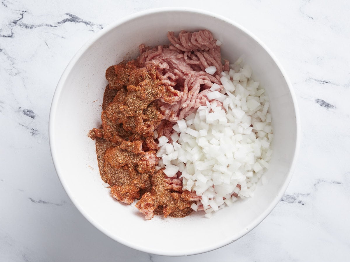 Ground beef and pork in a bowl with diced onion.