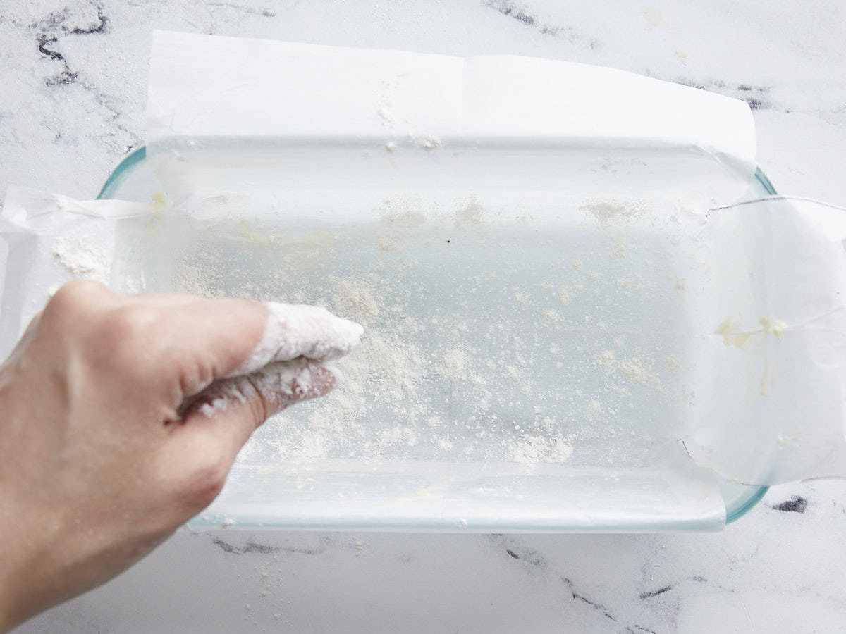 Loaf pan being buttered and dusted with flour. 