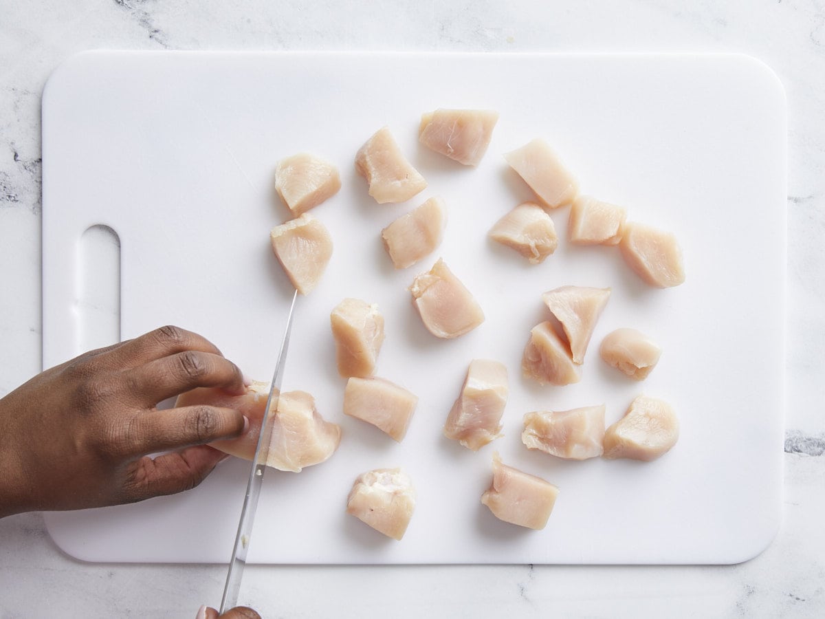Chicken breast being cut into 1 inch pieces on a cutting board
