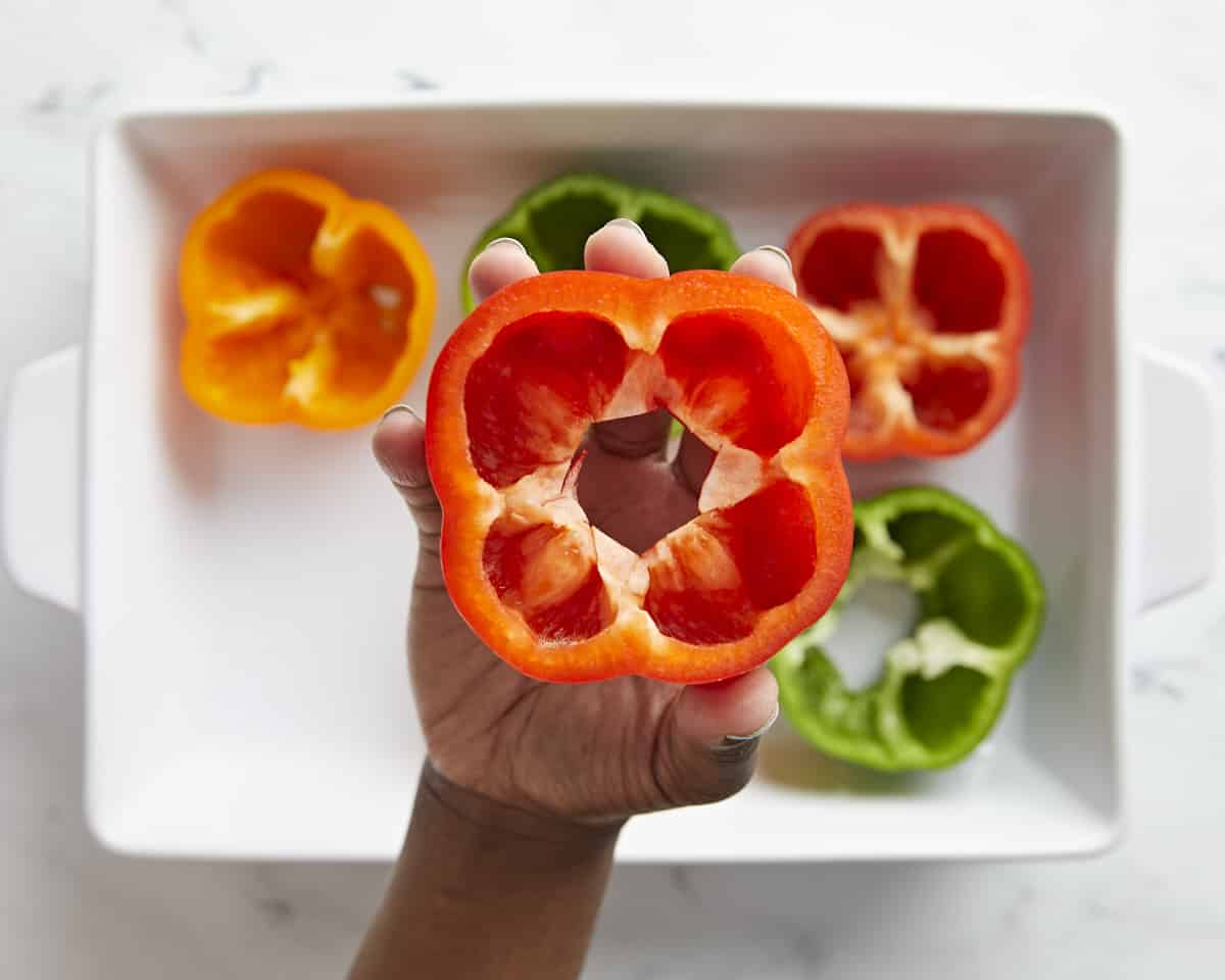 Bell peppers cut in half and placed in a casserole dish. One bell pepper lifted up towards the camera.
