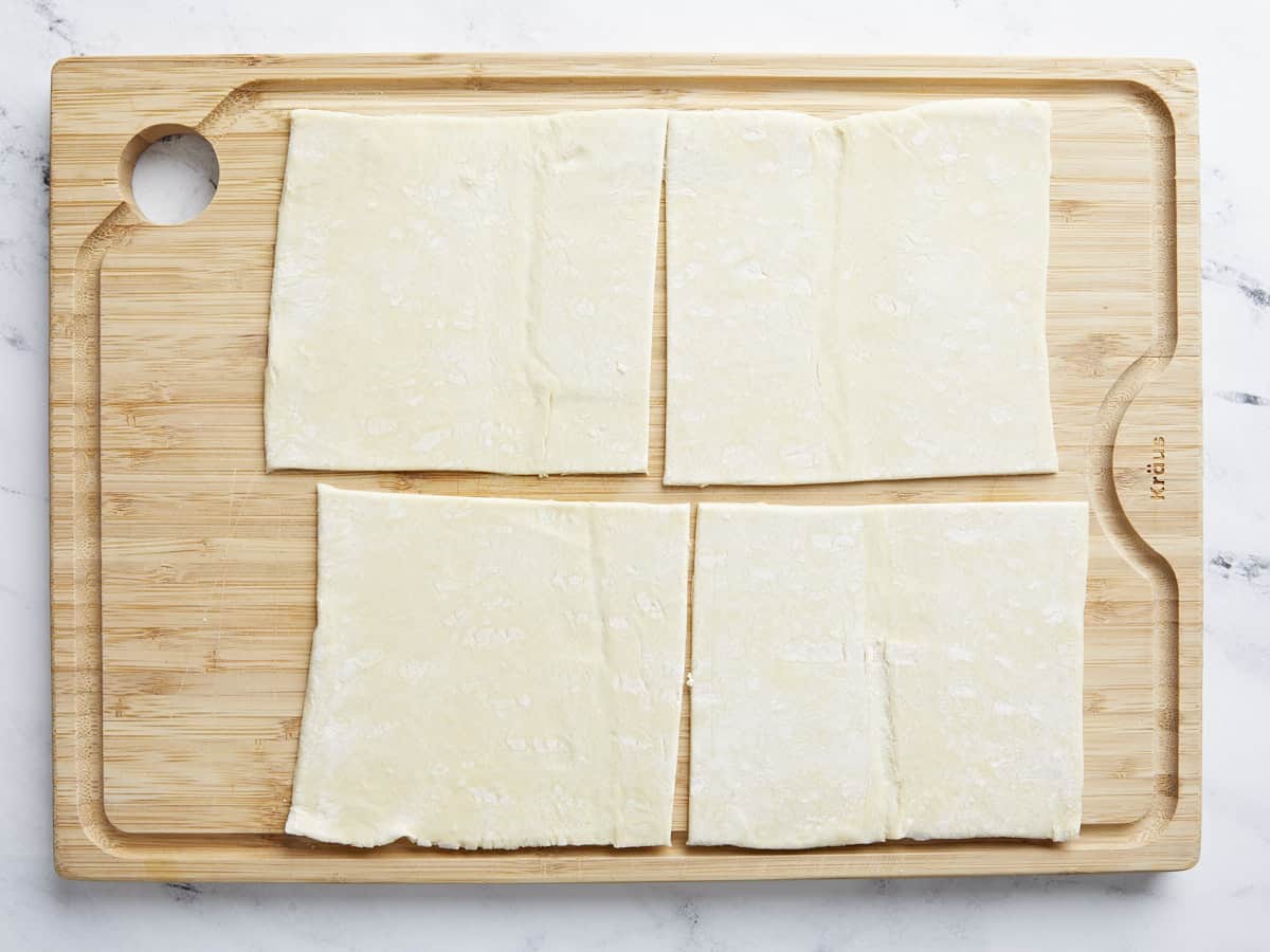 Puff pastry cut into squares on a cutting board.
