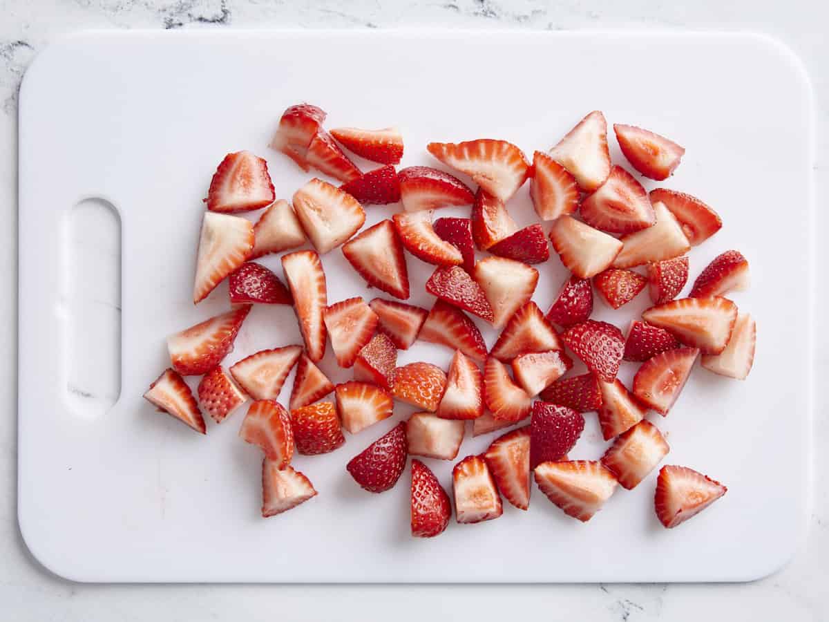 Chopped strawberries on a white cutting board.
