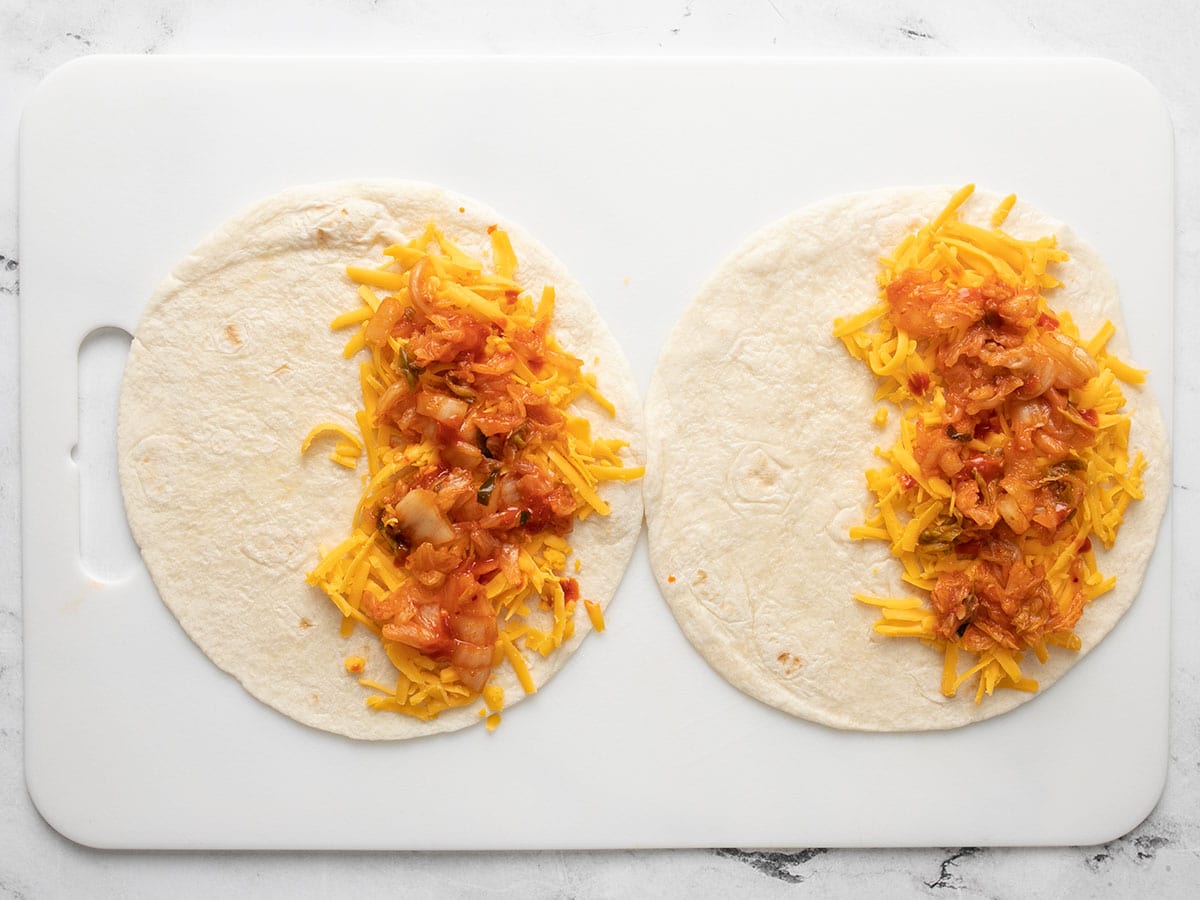 Cheese and kimchi covering half of two tortillas.