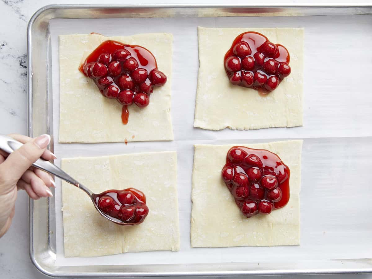 Cherry filling being spooned onto puff pastry squares.