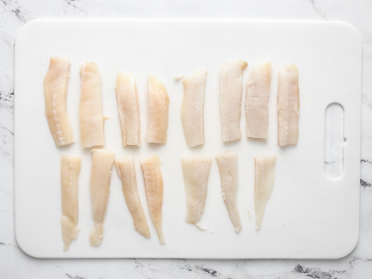 Fish filets cut into fish sticks on a cutting board.