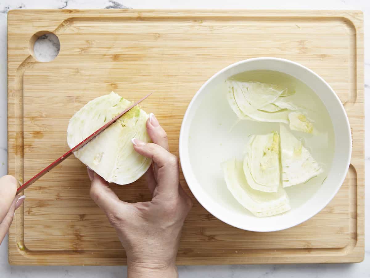 Overhead shot of a fennel bulb being sliced on a cutting board.