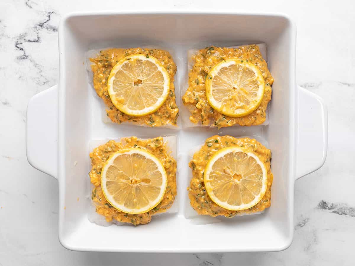 Lemon slices placed on top of fish in the baking dish.