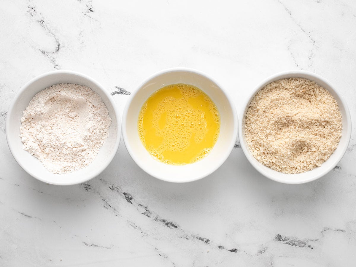 Three bowls with ingredients for the breading (flour, eggs, breadcrumbs).