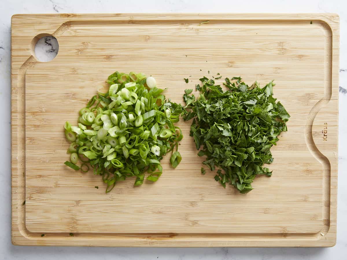 Overhead shot of sliced green onions and parsley on a cutting board.