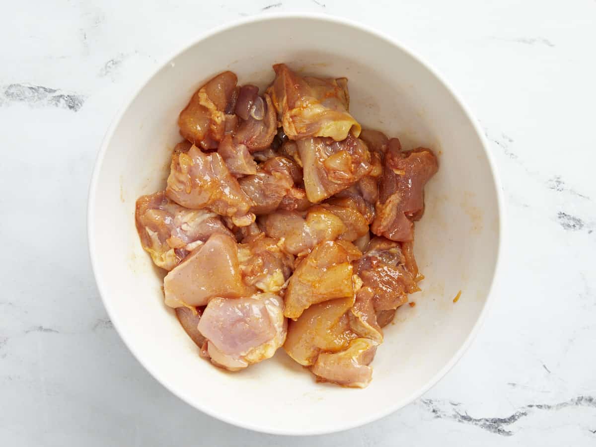 Overhead shot of cut chicken marinating in a white bowl.