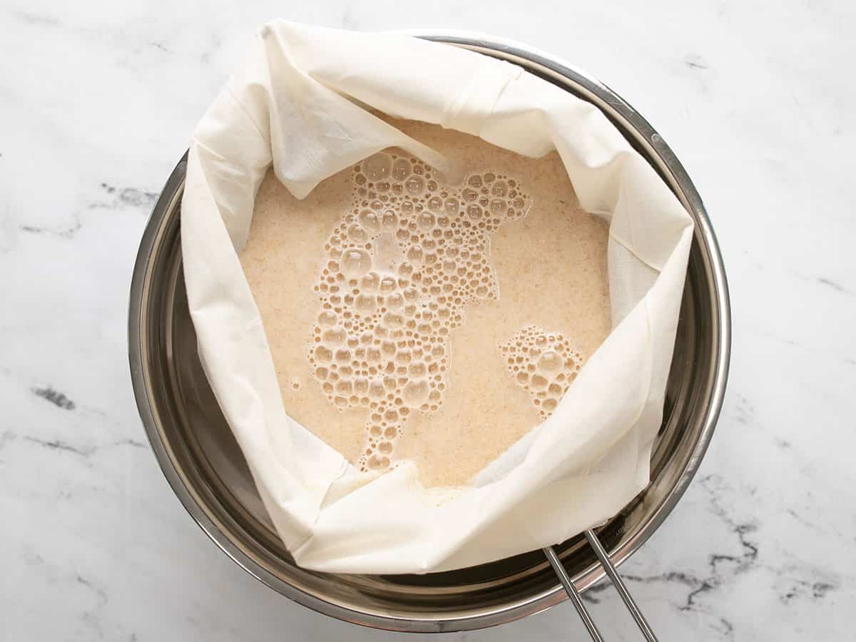 Oat milk poured into a nut bag over a strainer and bowl.