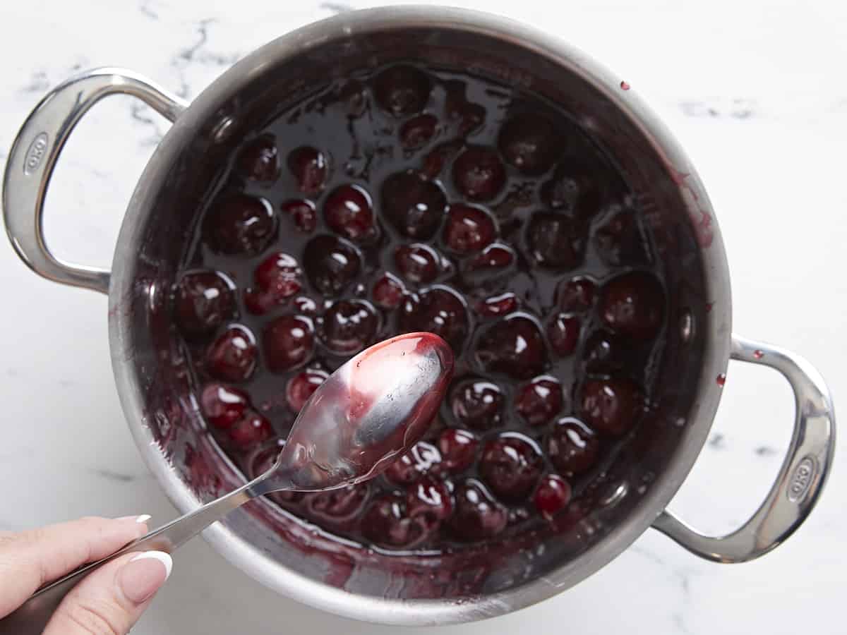 Finished cherry sauce coating the back of a spoon.