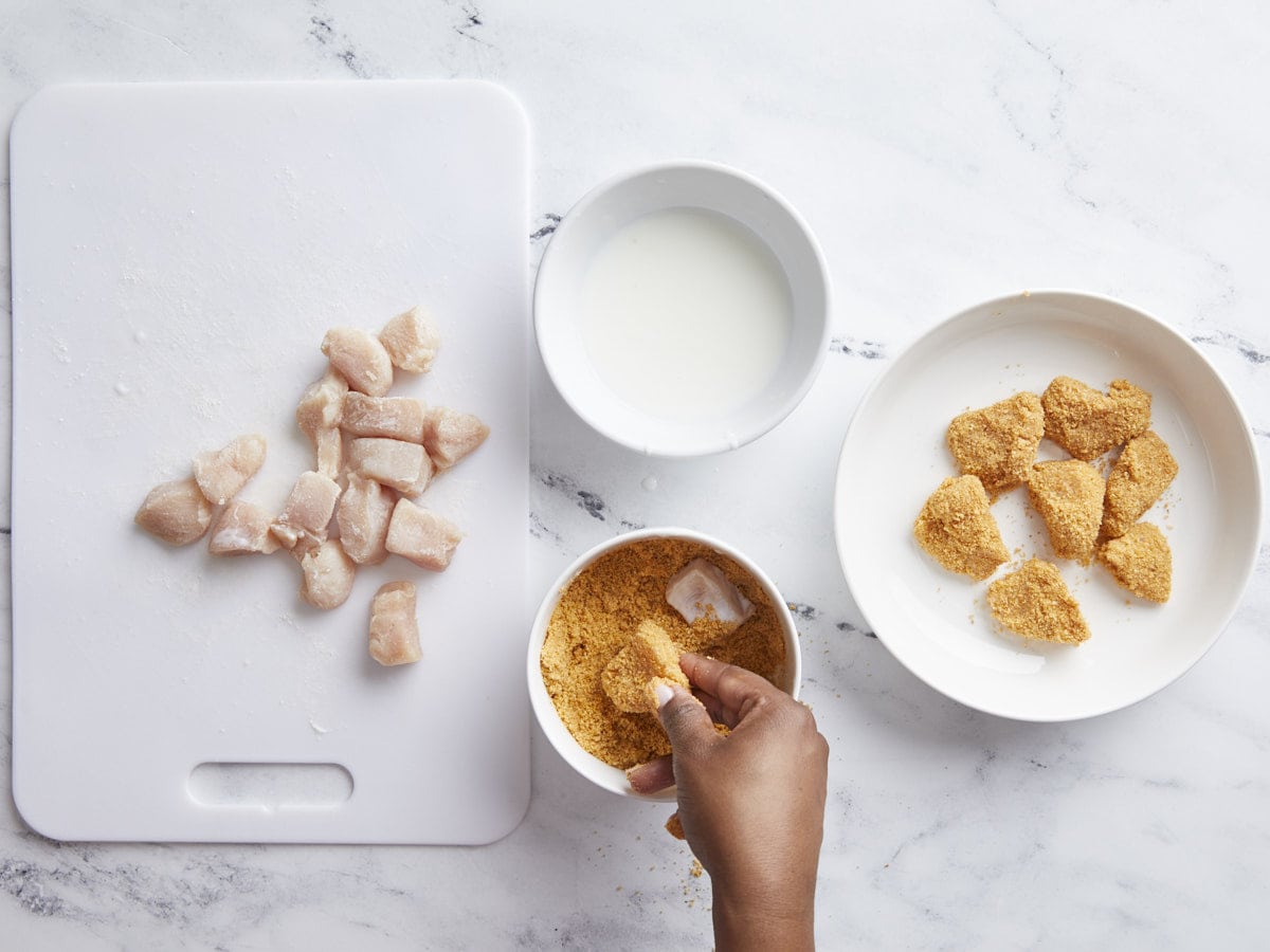 Chicken nugget assembly line with chicken pieces on the left, buttermilk and breadcrumbs in the middle, and coated chicken nuggets on the right.